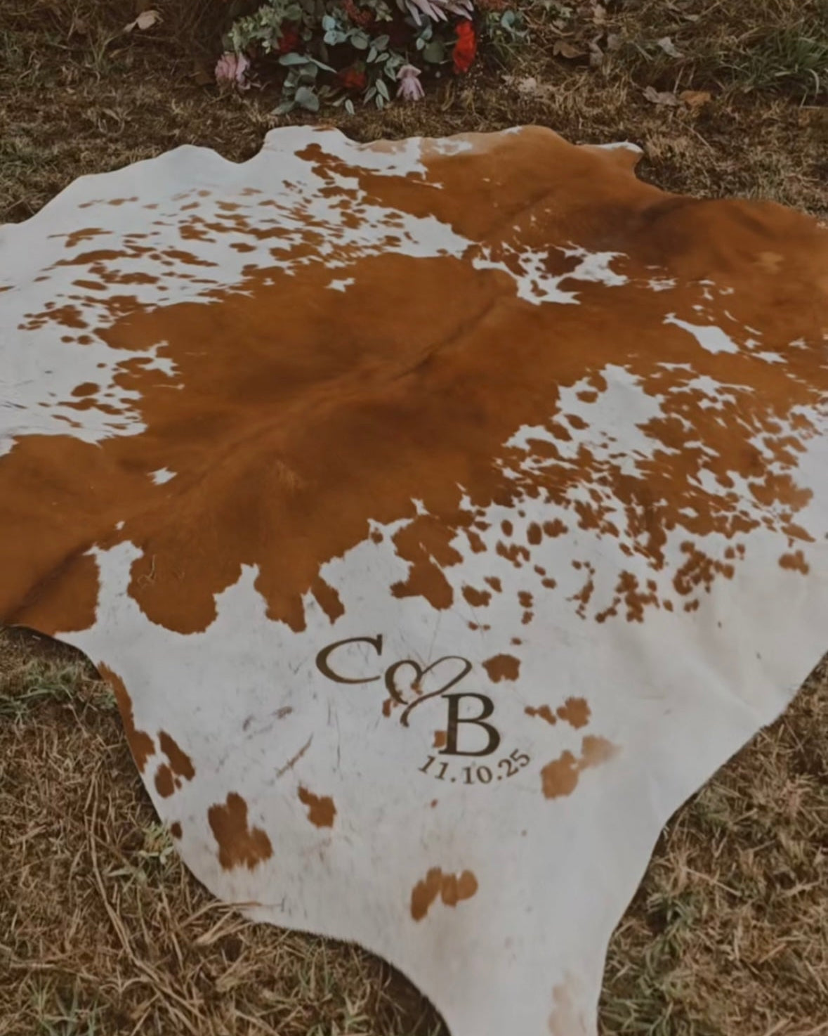Cowhide rug with monogram and date on a grassy background